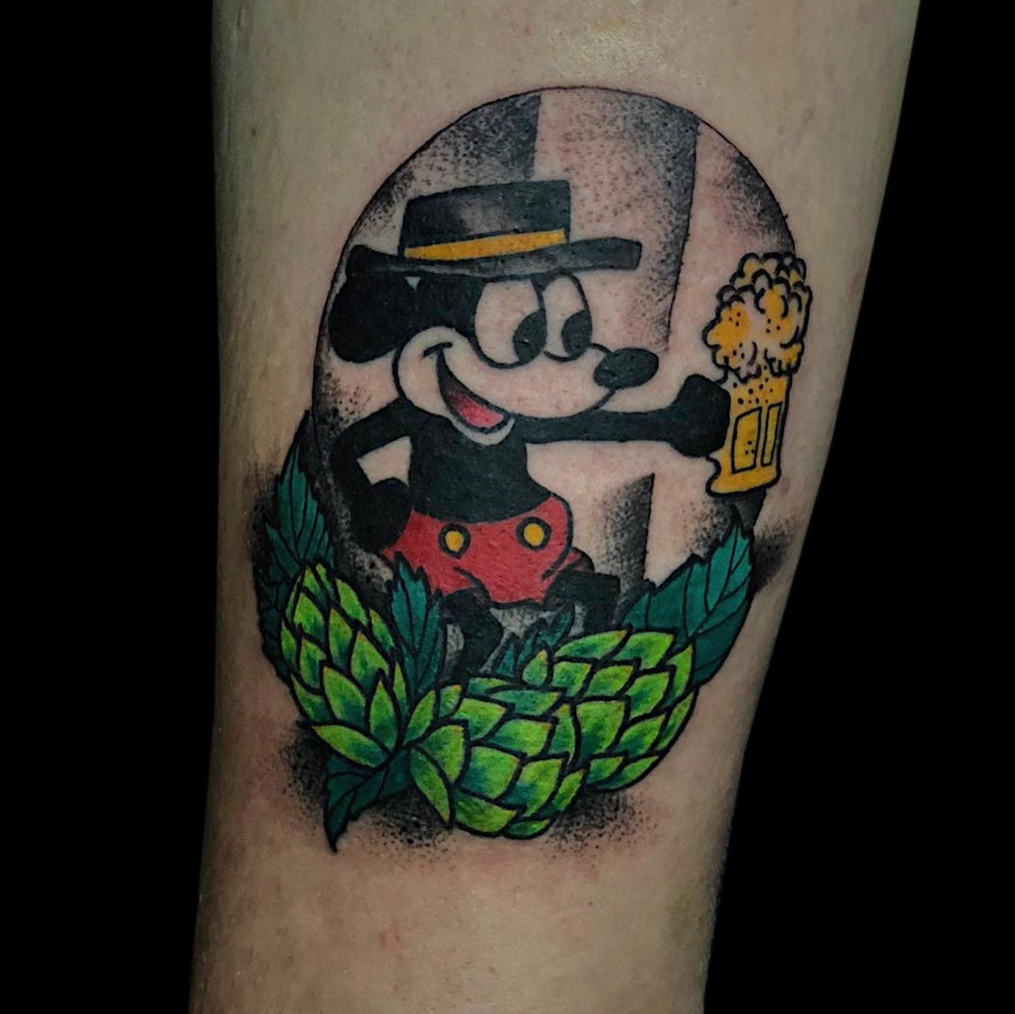 Colorful tattoo of an old-school style Mickey Mouse holding a beer mug, surrounded by green hops